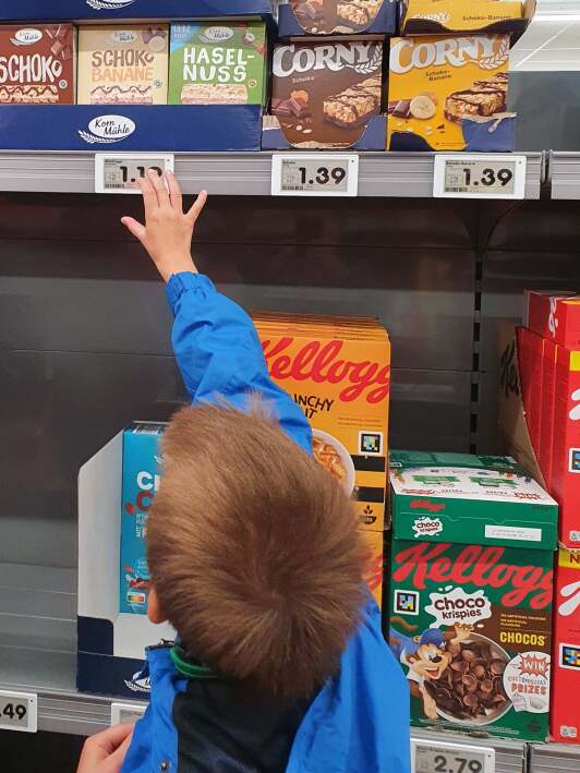 Junge greift nach Cornflakespackung im Supermarkt