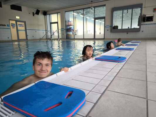 Schüler in der Schwimmhalle am Beckenrand mit Schwimmbrettern