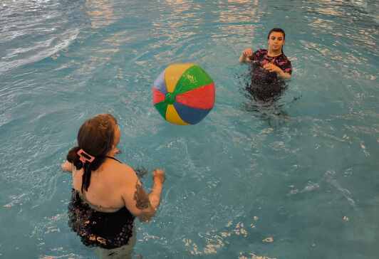 Schülerin mit Lehrkraft im Schwimmbecken mit buntem Wasserball