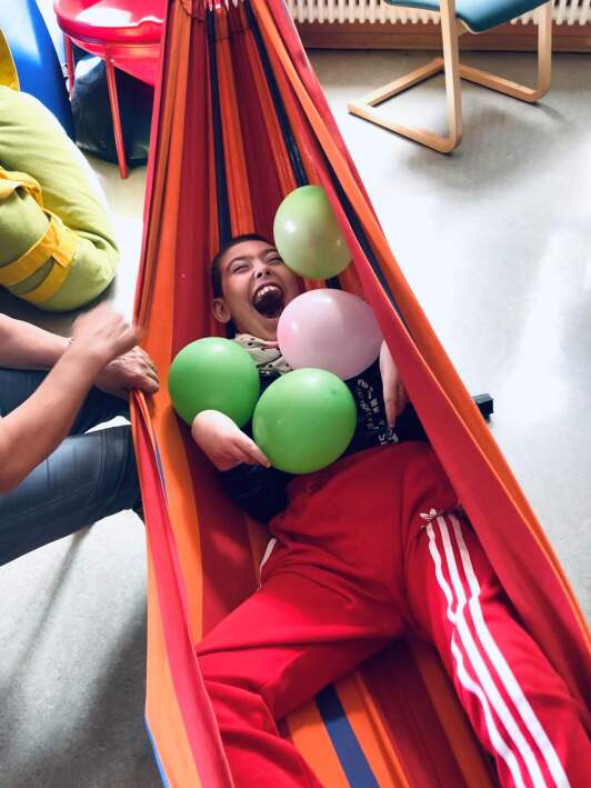 Schüler liegt mit bunten Luftballons in einer Hängematte