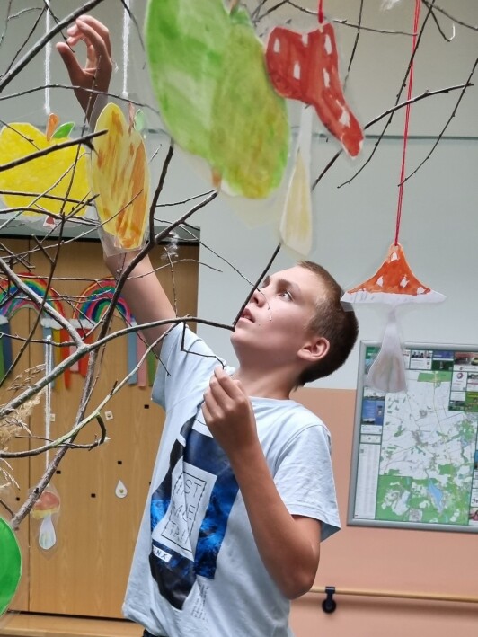 Schüler hängt selbstgestaltete Herbstblätter an einen Baum