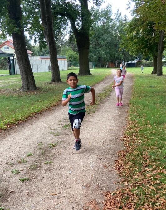 5 Schüler rennen auf dem Sportplatz den Sandweg entlang.